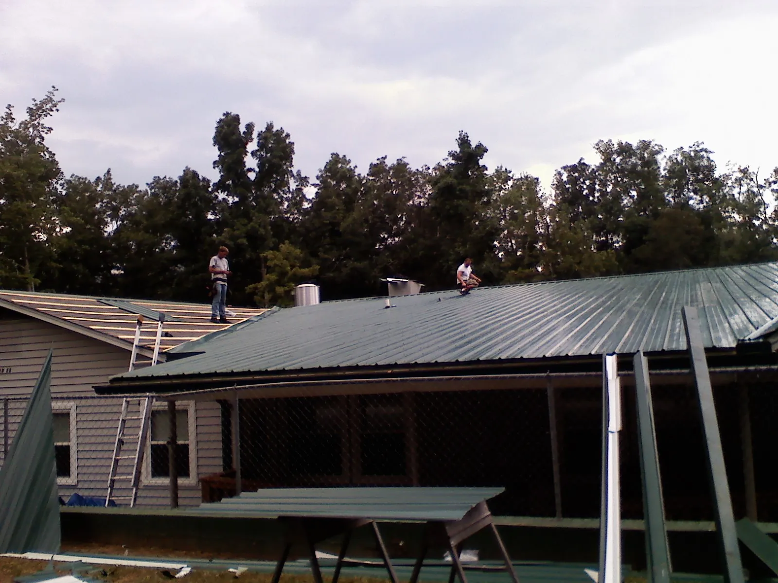 Two roofers installing green metal panels above a covered porch in North Salem