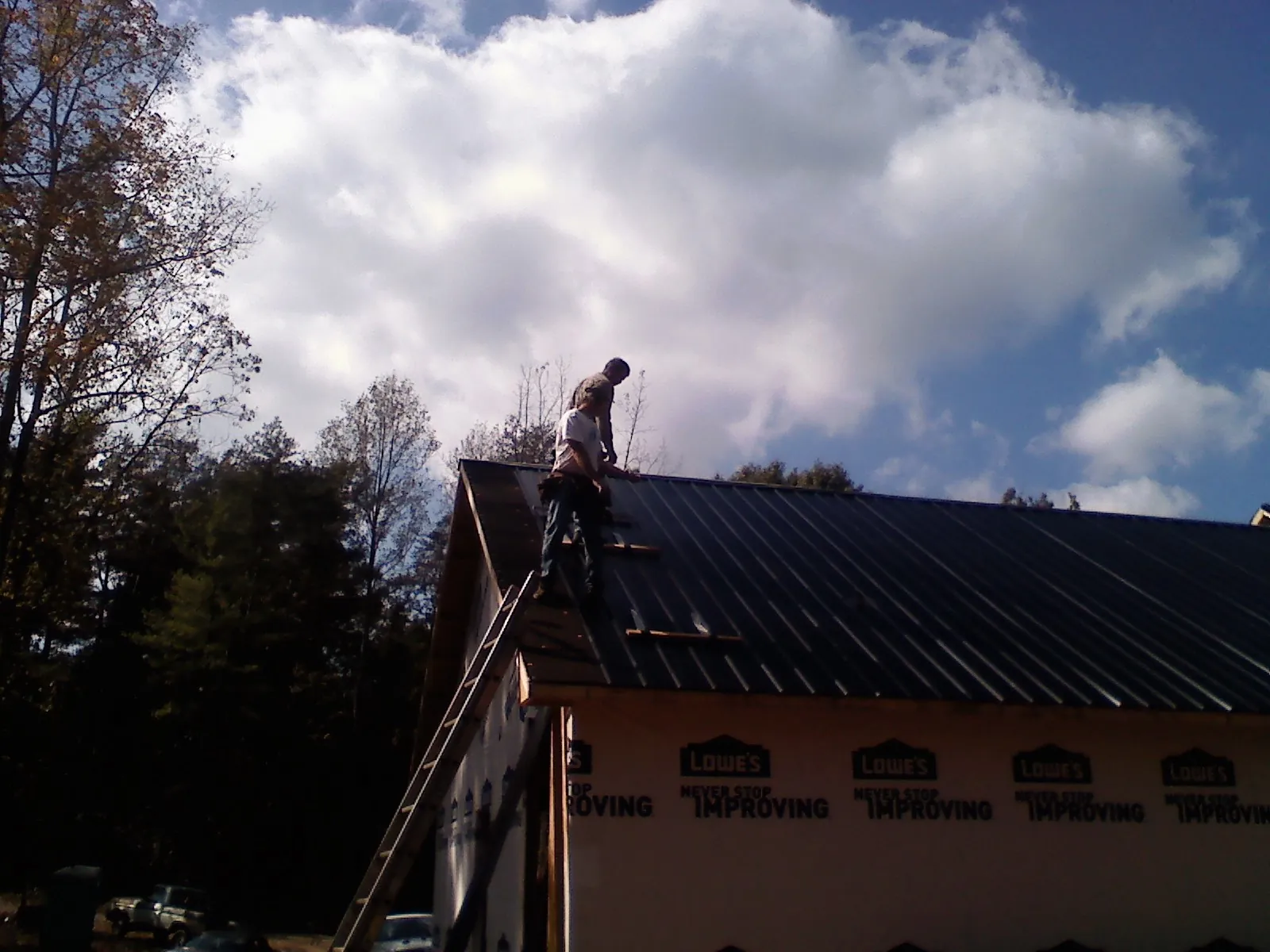 Roofer fastening dark metal panels high against a cloudy sky, from a Roof Inspection job in North Salem