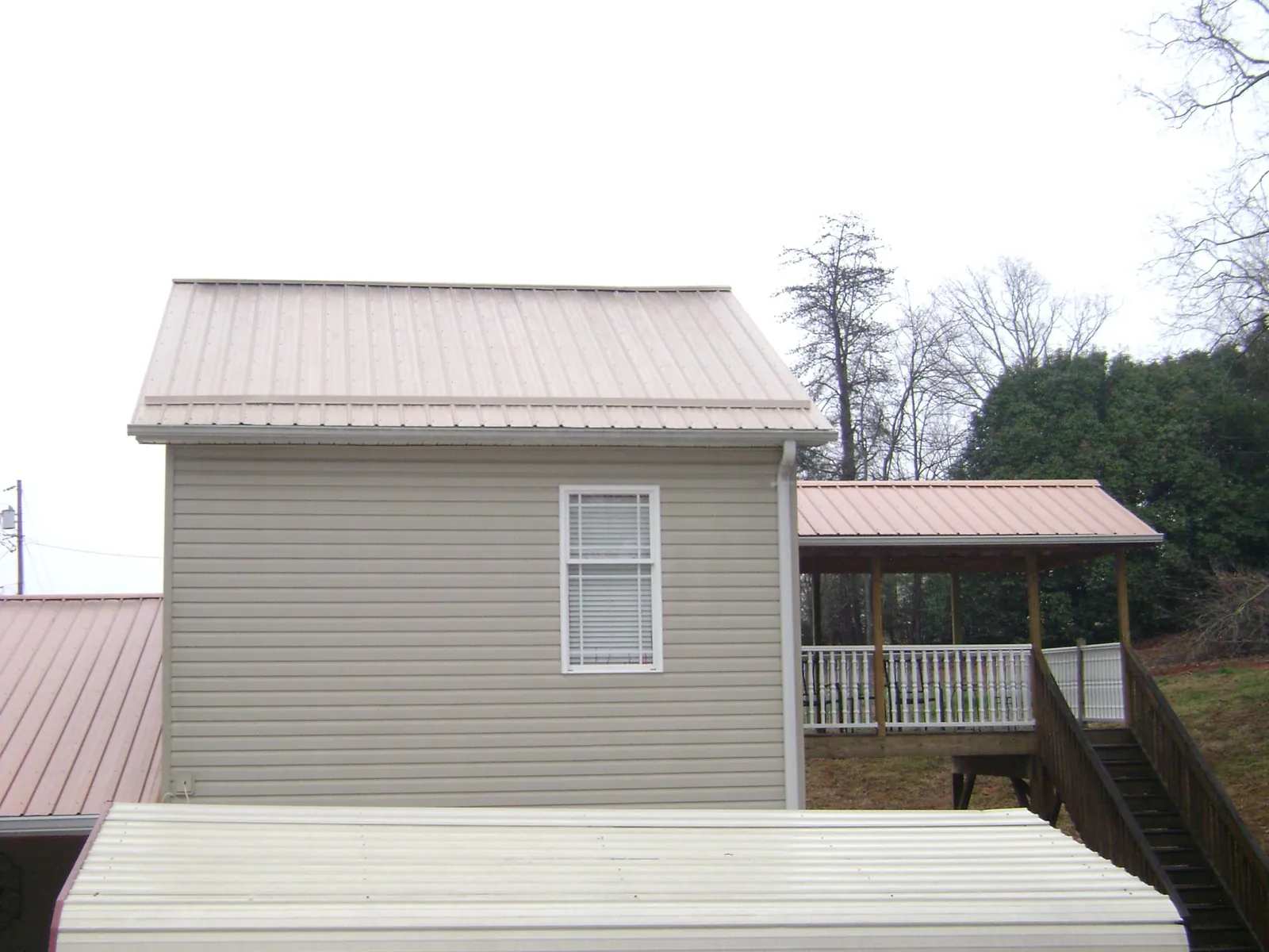 Tan metal roofs on a two story addition and attached porch, from a Roof Replacement job in North Salem